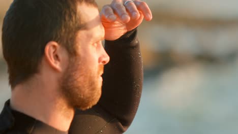 Vista-Lateral-De-Un-Surfista-Caucásico-De-Mediana-Edad-Mirando-El-Mar-En-La-Playa-4k