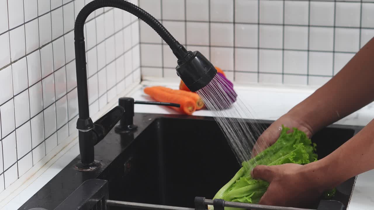 Hænder vasker frisk salat og grøntsager i en køkkenvask.