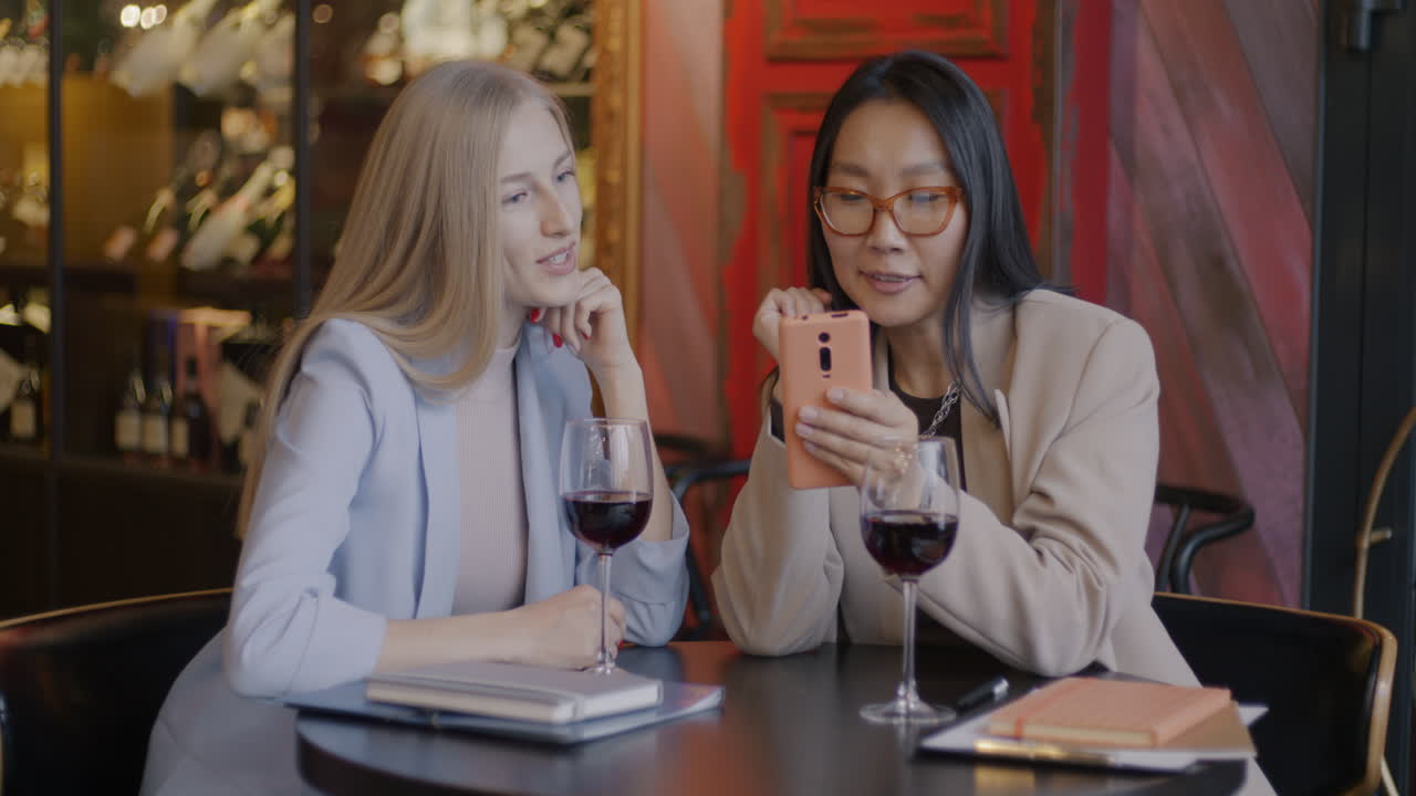 Businesswomen enjoying a drink and looking at their phone in a cafe
