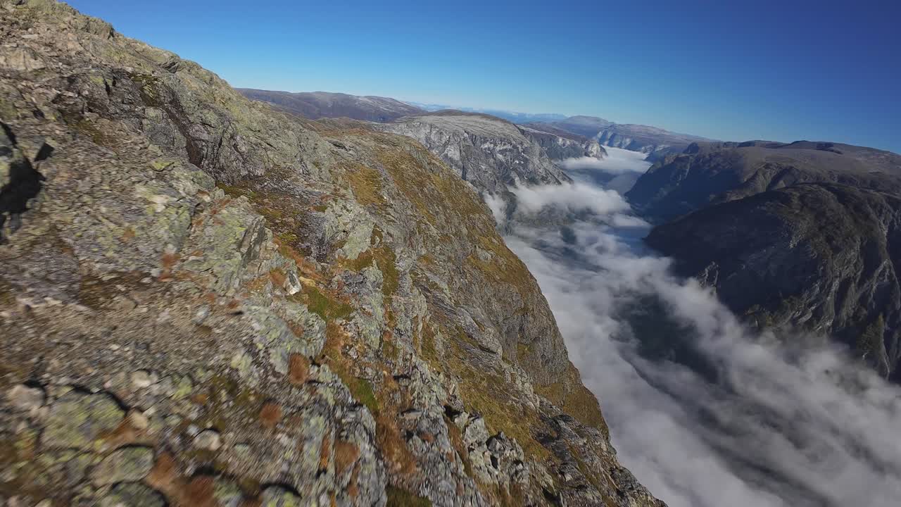 FPV drone flies fast and close to Bakkanosi mountain and rocks, revealing breathtaking fjord views far below