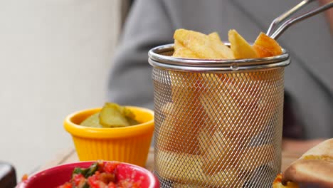 close up of a hand reaching for a french fry from a basket.