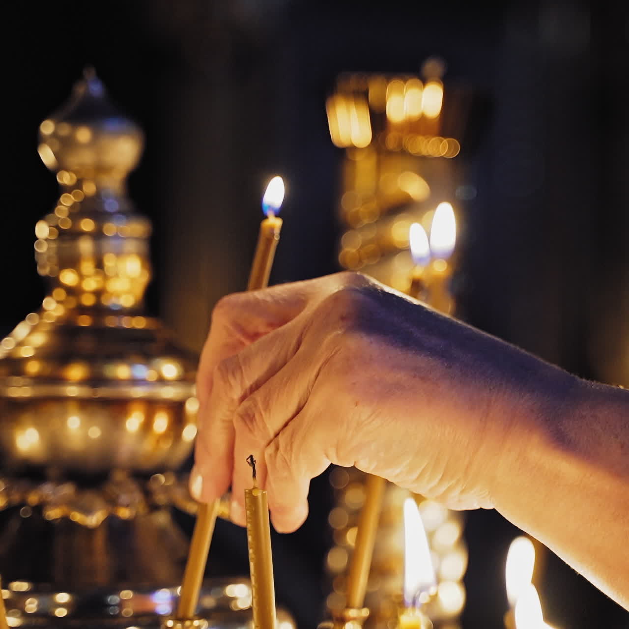 Female's hand is lighting a yellow candle in church. Burning candles in the night temple during worship. People put glowing candles for prayer intentions.