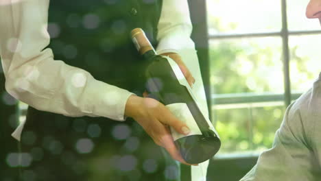 animación de luces sobre la sección media del camarero con una botella de vino y una pareja caucásica en un restaurante