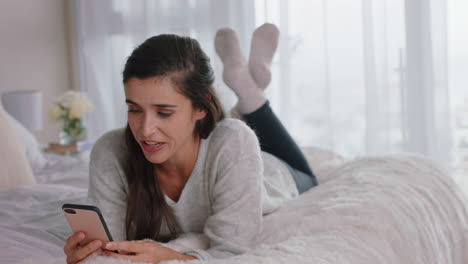 Hermosa-Mujer-Teniendo-Video-Chat-Usando-Un-Teléfono-Inteligente-Charlando-Con-Un-Amigo-Disfrutando-De-Una-Conversación-Acostada-En-La-Cama-Relajándose-En-Casa