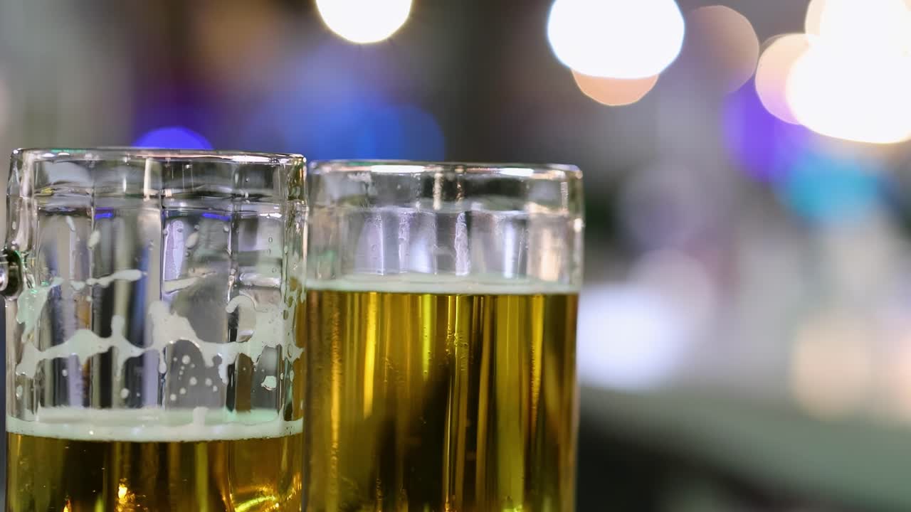 Two beer glasses on a counter with colorful, blurred bokeh lights in the background.