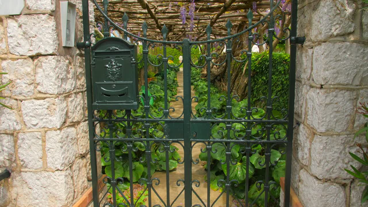 Iron Gate Through Botanical Gardens Of Villa Della Pergola With Growing Wisteria Vines In Capri, Italy