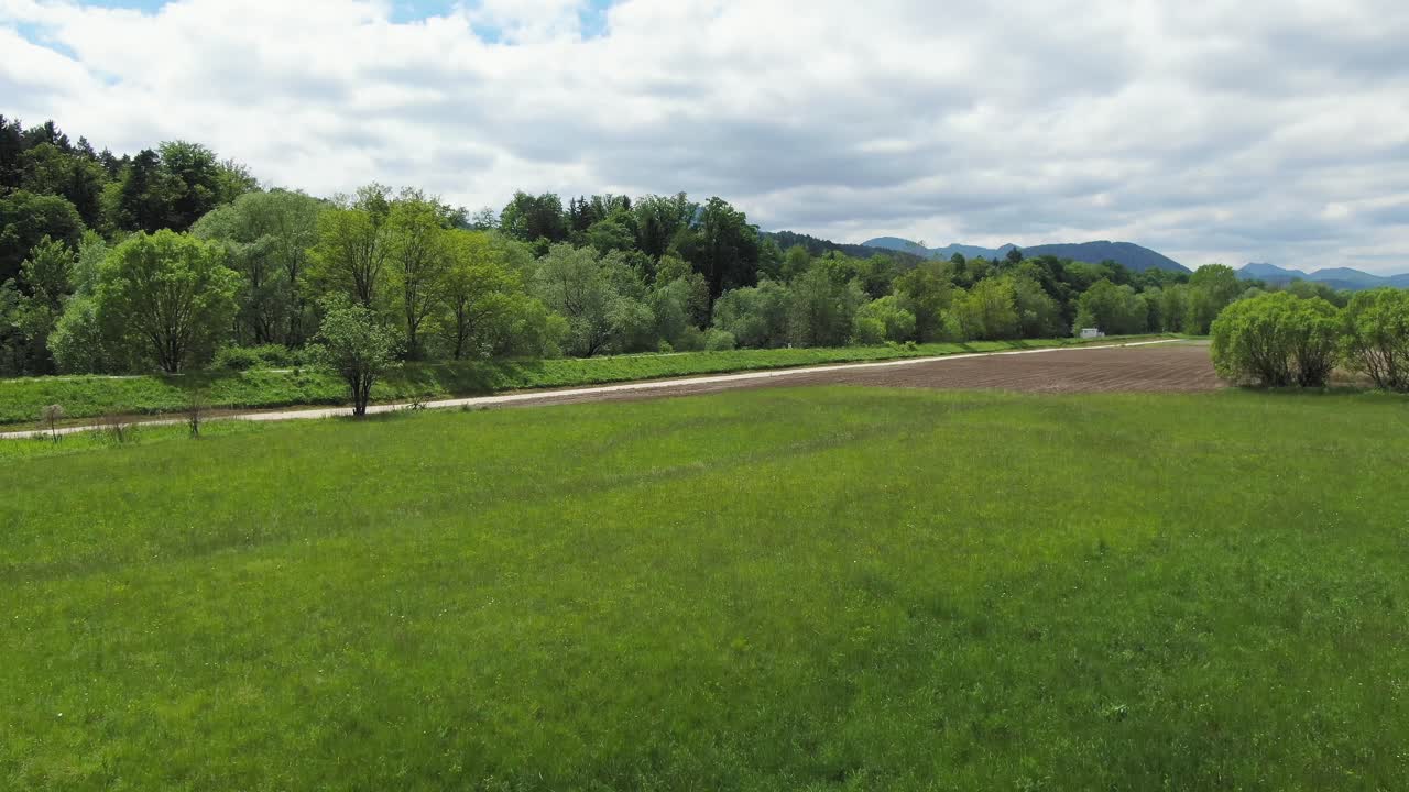 Fast drone flies low over green grass toward river and turns quickly right