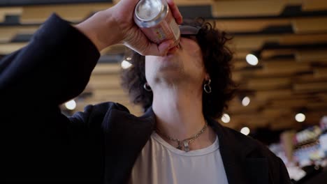 Confident-and-cool-guy-with-curly-black-hair-in-black-sunglasses-drinks-lemonade-and-wipes-his-mouth-with-his-hand-while-shopping-in-a-supermarket