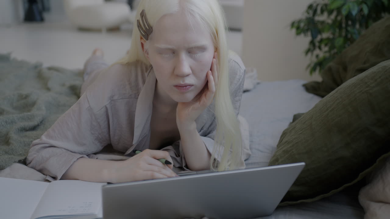 Young woman studying on a laptop in bed