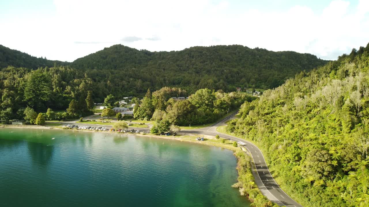 campamento de vacaciones junto al lago, lago azul, camino del bosque de palmeras y turista en paddle bord 4k drone disparado en nueva zelanda