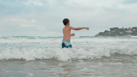 Niño-Feliz-Divirtiéndose-En-La-Costa.-Chico-Despreocupado-Bailando-En-El-Agua-A-La-Orilla-Del-Mar.