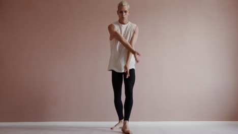 a young man in a white tank top and black leggings dances in a studio