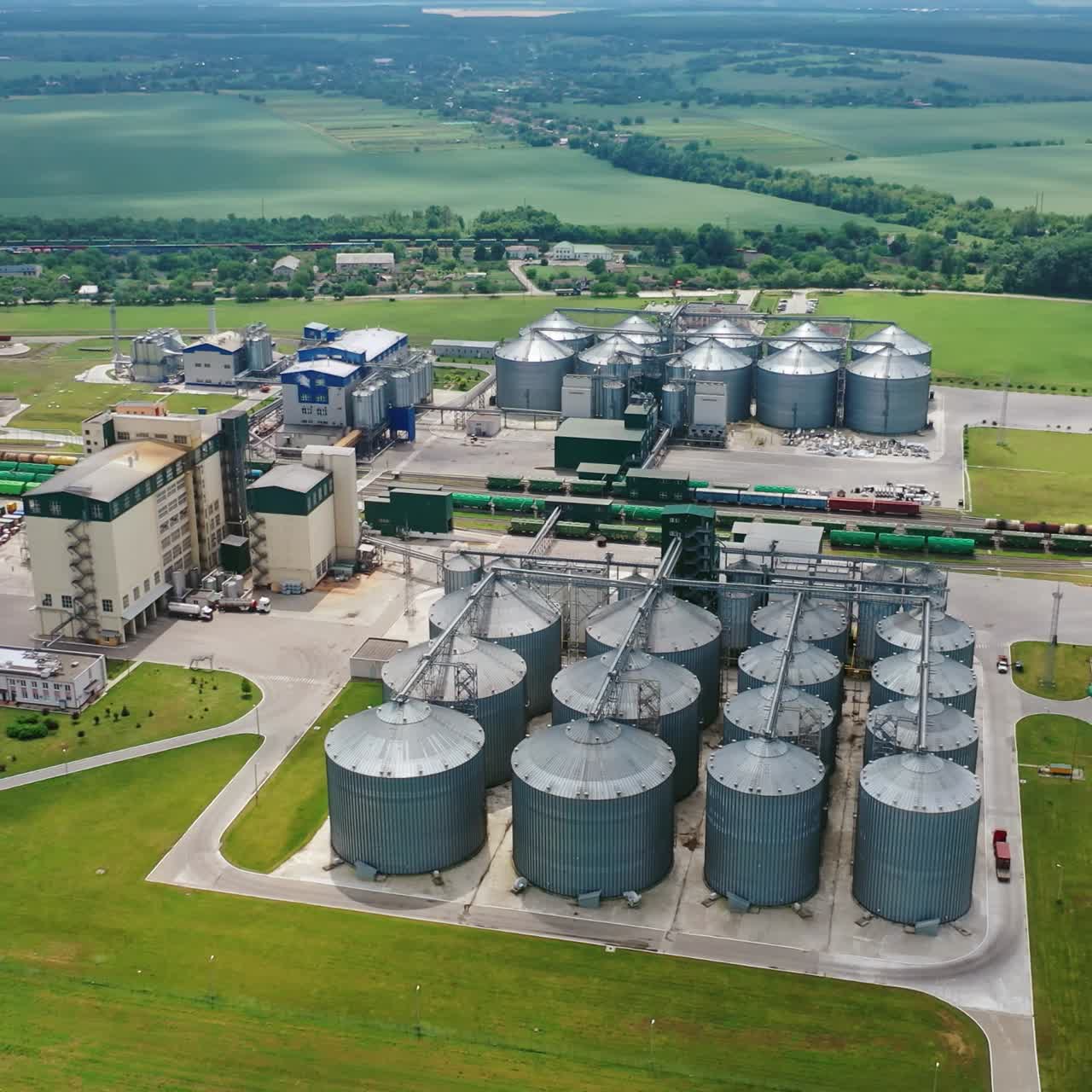 Innovative agriculture factory in nature. Modern grain silos elevators on green field in summer. Steel granary. Aerial view.