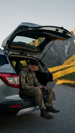man works on laptop from car trunk in scenic mountain landscape