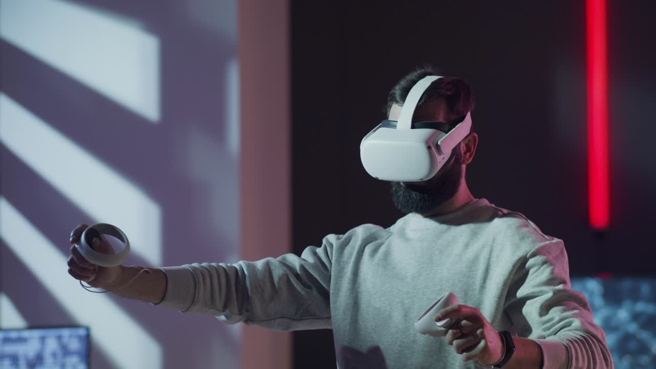 Side view of a bearded man using a VR headset and controllers. He makes creative gestures as if designing or sculpting in an immersive virtual world, surrounded by neon lights.