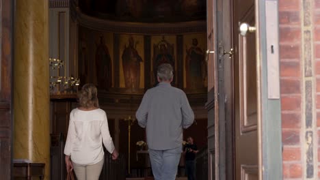 Older-couple-tourist-walking-into-old-church-holding-hands-Copenhagen-well-dressed