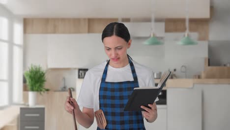 ama de casa india confundida haciendo comida a partir de un libro de recetas