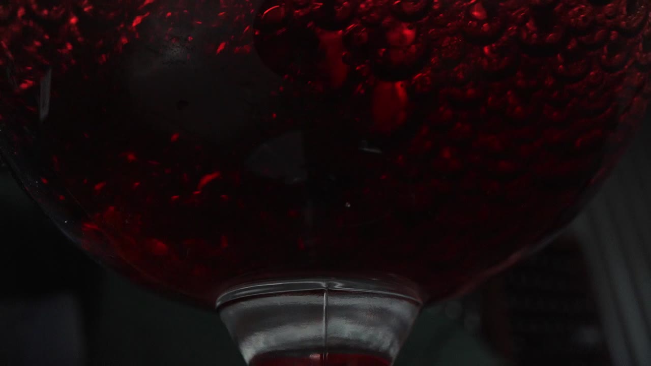 와인잔에 적포도주를 붓고 어두운 변덕스러운 배경으로 넓은 매크로 슬로우 모션을 닫습니다.