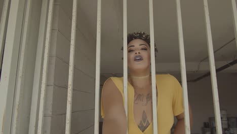 alternative tattooed woman in a yellow dress stretches out her hand in an attempt to touch the viewer through a white iron bars