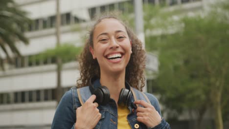 portrait of happy biracial woman in city, wearing headphones and smiling