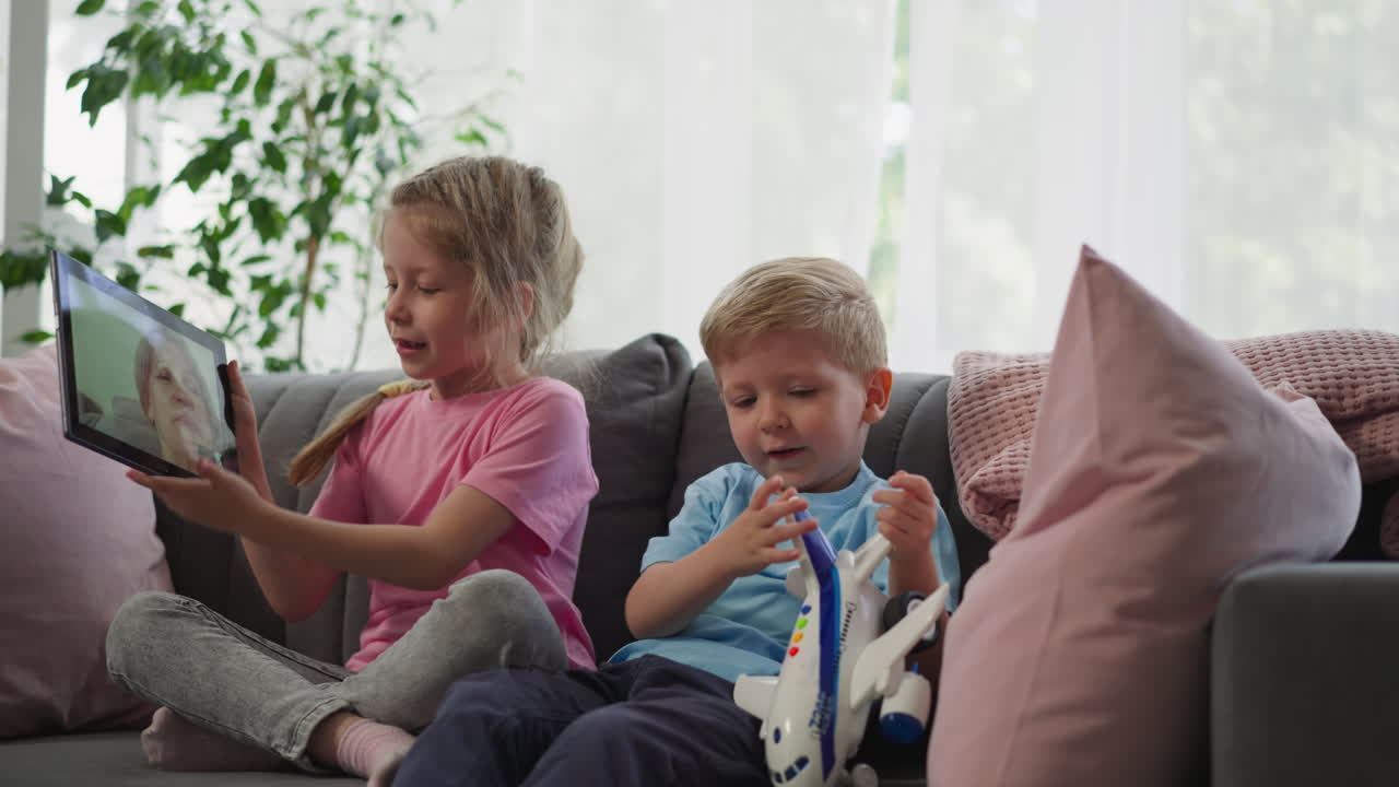 los hermanos hablan con la abuela en video llamada a través de la tableta en el sofá