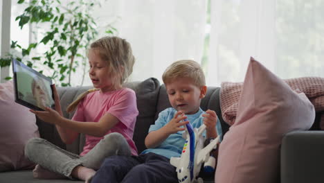 Geschwister-Sprechen-Mit-Oma-Per-Videoanruf-über-Tablet-Auf-Der-Couch