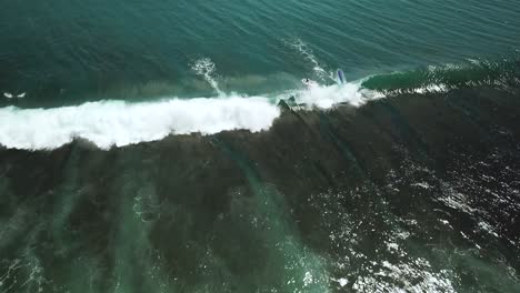 drone shot over two surfers failing to catch a wave at padang padang beach in bali, indonesia