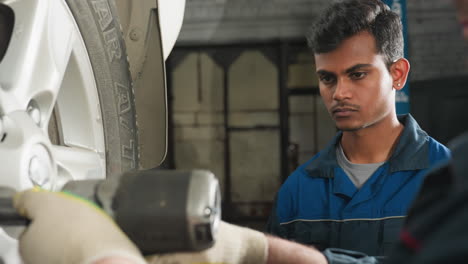 close-up head view of mechanic observing a colleague using a pneumatic tool to tighten car wheel bolts in a garage, teamwork and precision in automotive repair ensure proper wheel alignment