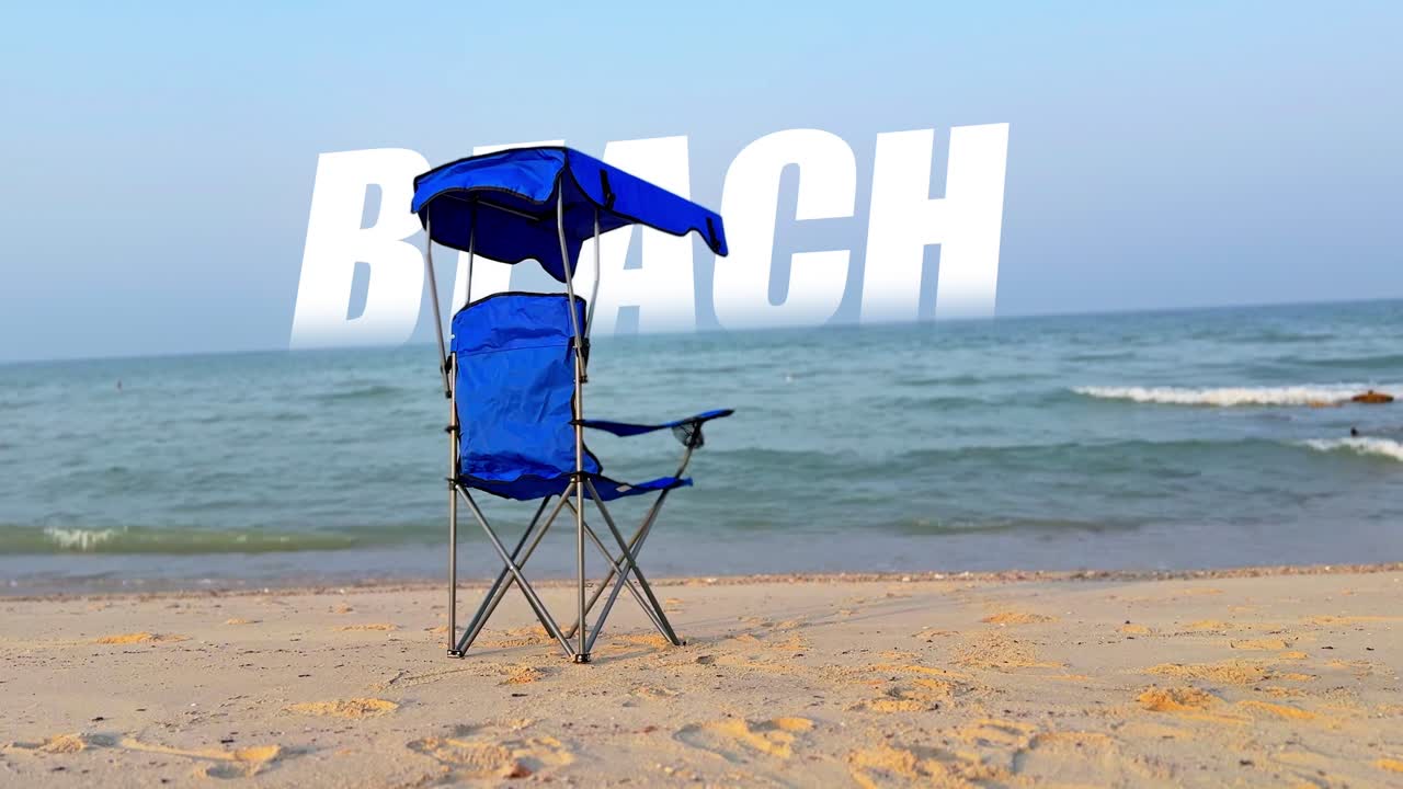 Relaxing shot of a blue folding chair on the sandy beach facing the ocean waves under a clear sky. Perfect for travel, lifestyle, summer, and vacation projects