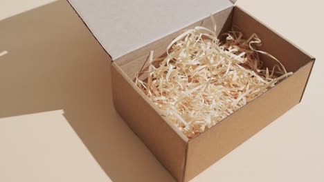video de una caja de cartón abierta con virutas de papel y espacio de copia sobre fondo marrón