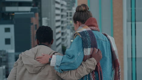 rear view happy friends on rooftop having fun together looking over edge enjoying view of urban city skyline watching people from roof at sunset