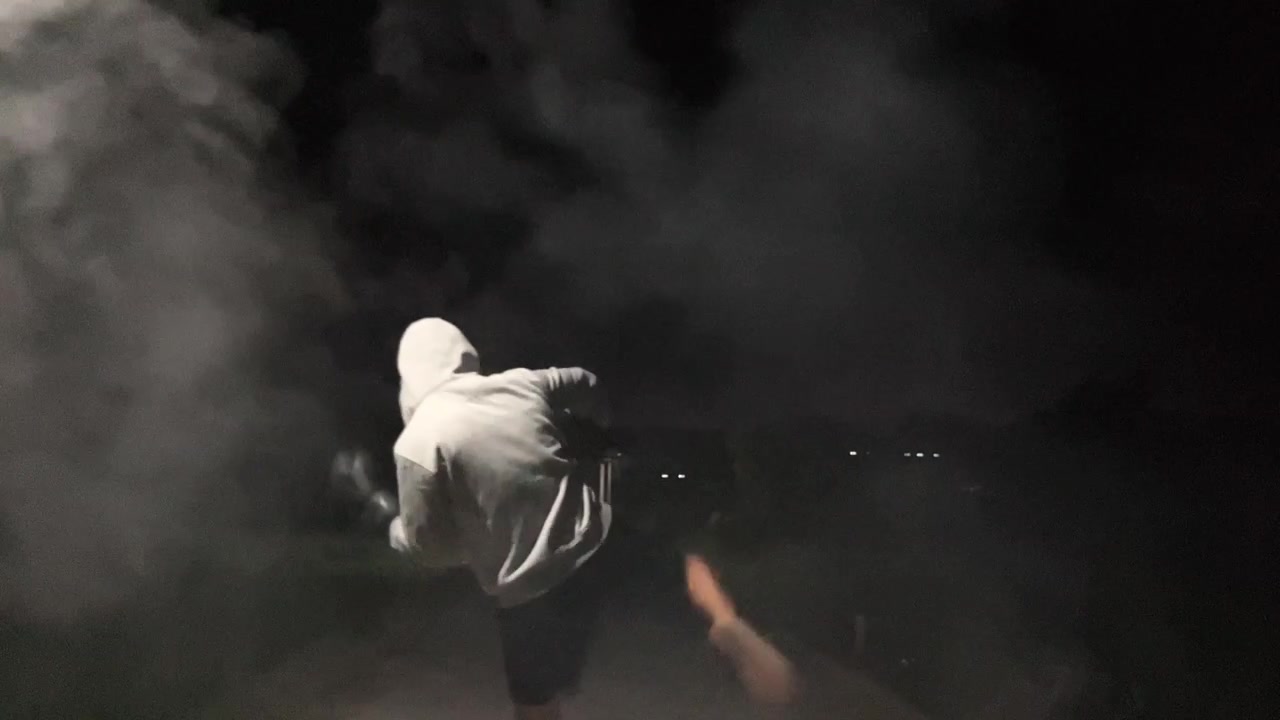 Slow motion cinematic clip of an anonymous man in a hoodie and boxing gloves practicing shadow boxing punches surrounded by thick smoke in the dark night. Intense athletic training.