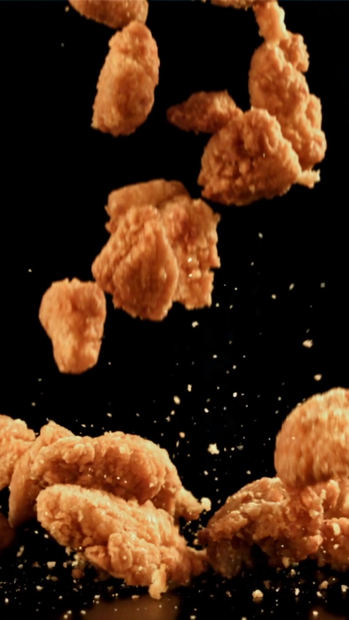 Nuggets di pollo fritti croccanti che cadono al rallentatore su sfondo nero