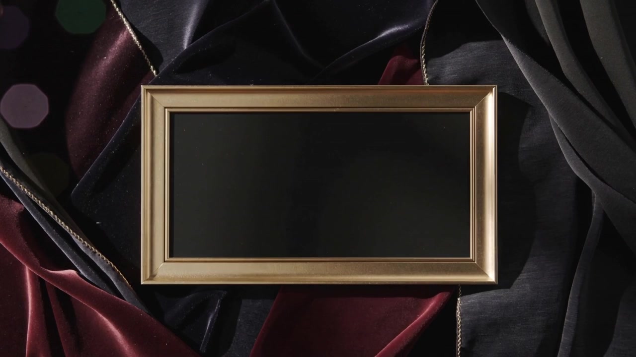 Přibližující se kamera ukazuje zlatý rám, černý panel se rozšiřuje v záběru, aby odhalil lesk, sametové lemování a bokeh.