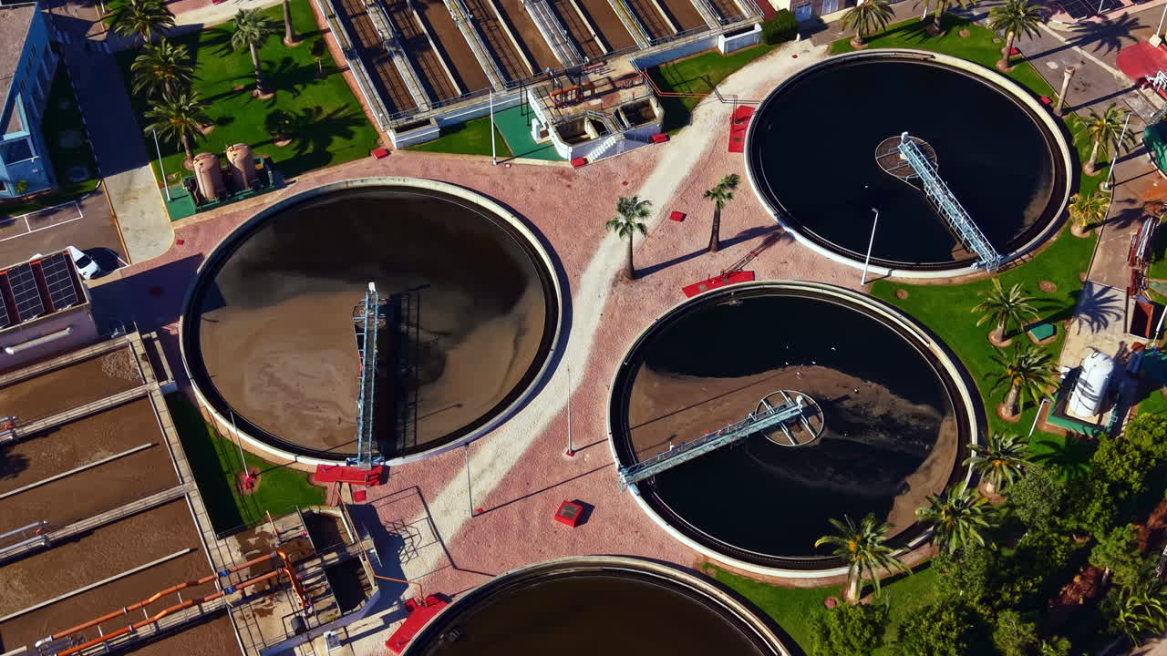 Planta de tratamiento de aguas residuales que opera con múltiples tanques en una zona soleada, mostrando el proceso de limpieza del agua para uso comunitario.