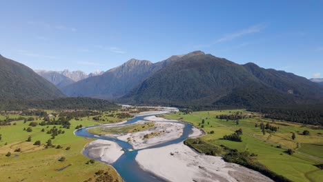 Alpine-river-meandering-through-rural-farmland-at-bottom-of-New-Zealand's-southern-alps-in-sunshine