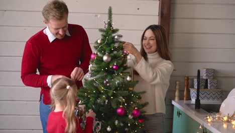 feliz pareja y su hija colgando la decoración de navidad en el árbol de navidad en casa