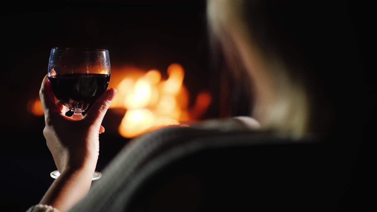 벽난로 옆에서 와인을 마시고 있는 여성의 어깨 너머로 보기