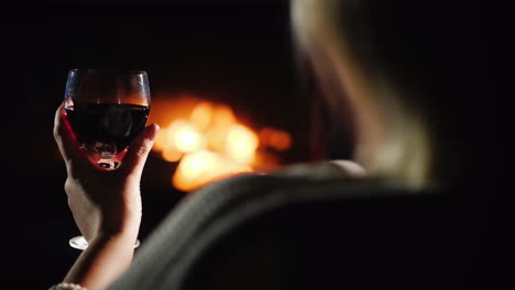 view over the shoulder of a woman with a glass of wine basking by the fireplace