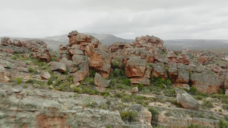 Drone flies over desert landscape and through rock formations in Cederberg Wilderness Area in South Africa with wide view of mountain range and desert landscape