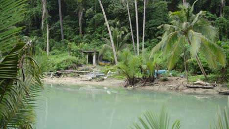 Ruhiges-Fischerdorf-Mit-Hütten-Und-Booten-Am-Schlammigen-Ufer-Einer-Breiten-Flussmündung-Im-Tropischen-Wald