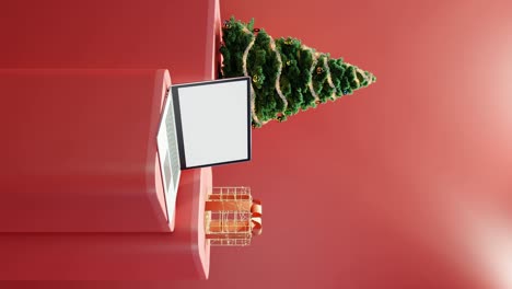 computadora portátil, árbol de navidad y regalo envuelto sobre fondo rojo vertical
