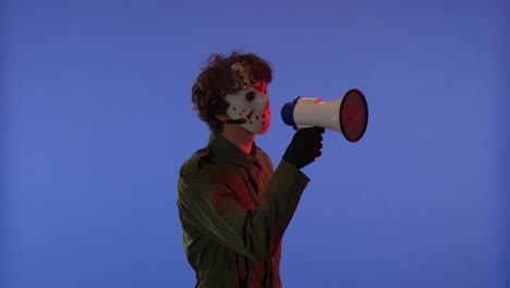 man in white mask with loudspeaker in hands on blue background with red neon light image of maniac