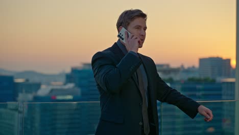 a happy caucasian businessman with a toothy smile talks on his smartphone in slow motion, with the seoul cityscape and sunset in the background from a rooftop