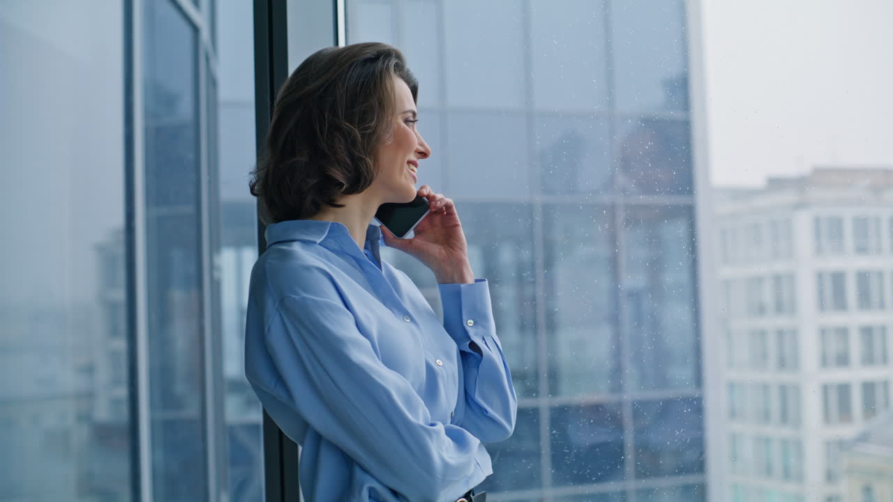 Smiling ceo talking mobile phone standing panoramic window closeup. Happy woman