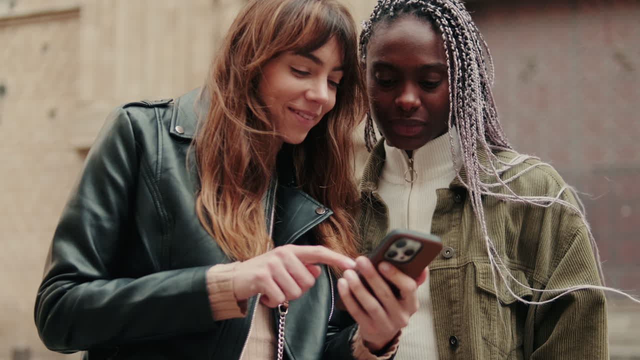 Two Diverse Young Women Smiling and Sharing Content on a Smartphone