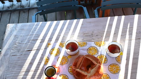 view of a tea party on a wooden table, hot cups of tea and a brioche, sunbeams