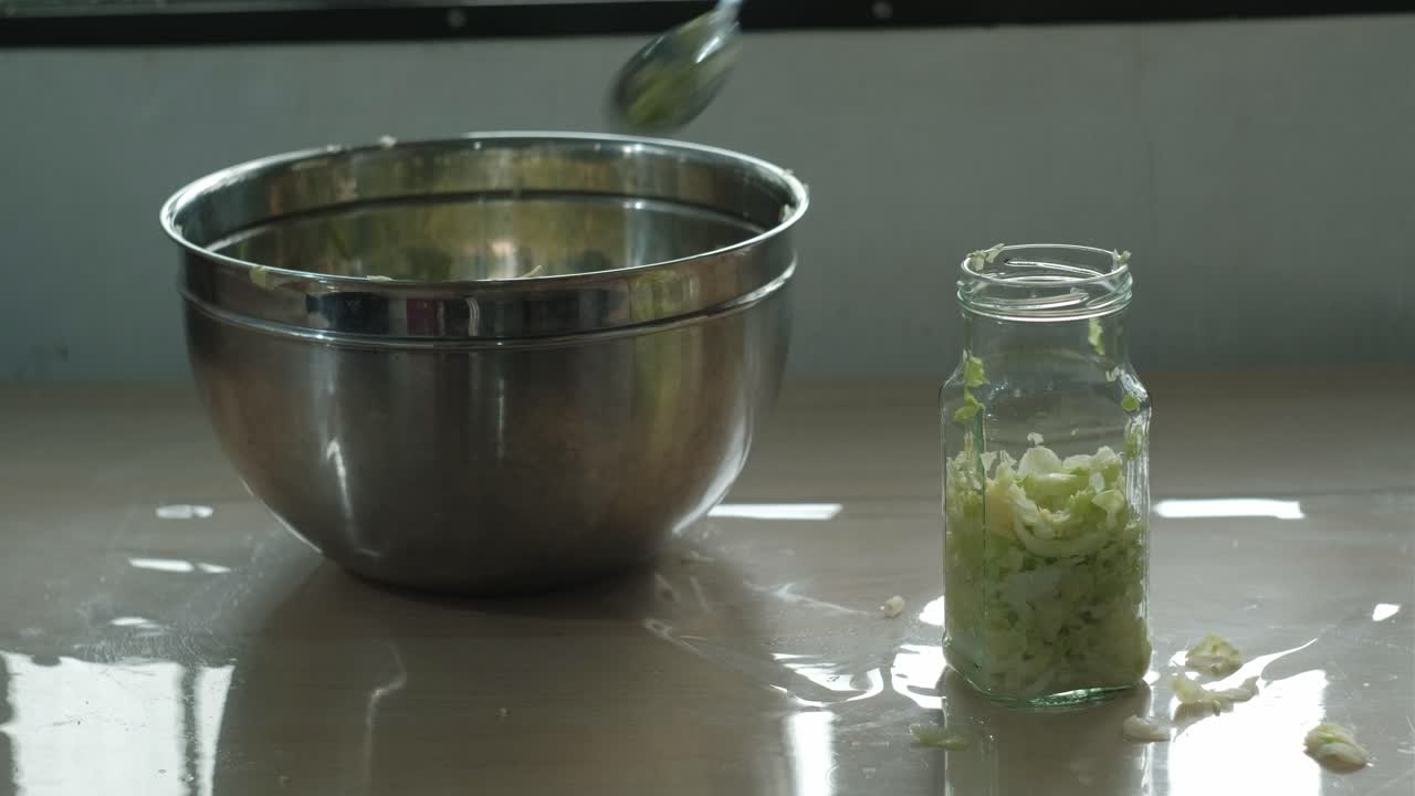 Person uses spoon to press and fill sauerkraut mix into glass jar for fermentation
