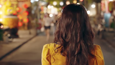 Mujer-Vestida-De-Amarillo-Ao-Dai-Caminando-Por-La-Noche-En-Hoi-An,-Vibrantes-Luces-De-La-Calle-Que-Proyectan-Un-Brillo-Festivo