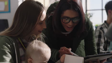 happy-caucasian-business-woman-mother-discussing-ideas-female-project-manager-using-digital-tablet-computer-sharing-project-information-on-screen-playful-baby-in-office-workplace